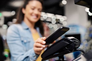 Donna sorridente paga con smartphone tramite POS contactless in negozio, esempio di partecipazione a concorsi a premi tramite acquisto in store.