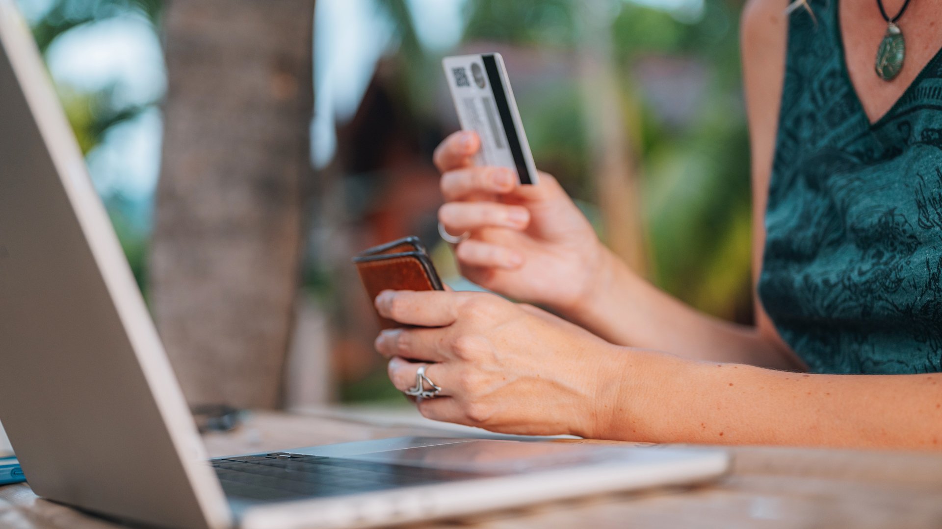 Persona che effettua un pagamento online con carta di credito e portafoglio davanti a un laptop.
