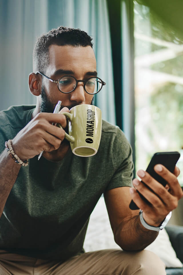 Uomo che sorseggia un caffé in una tazzina con la scritta MokaShop.